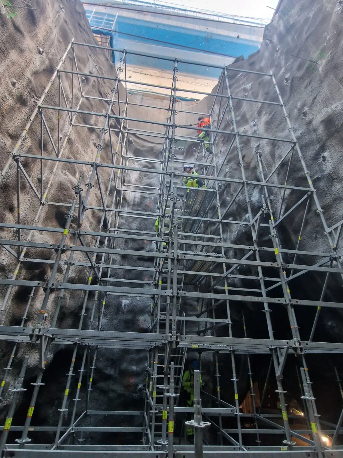Ställning i flera plan genom ett smalt bergschakt, sett nedifrån mot dagsljuset, med arbetare på trappan