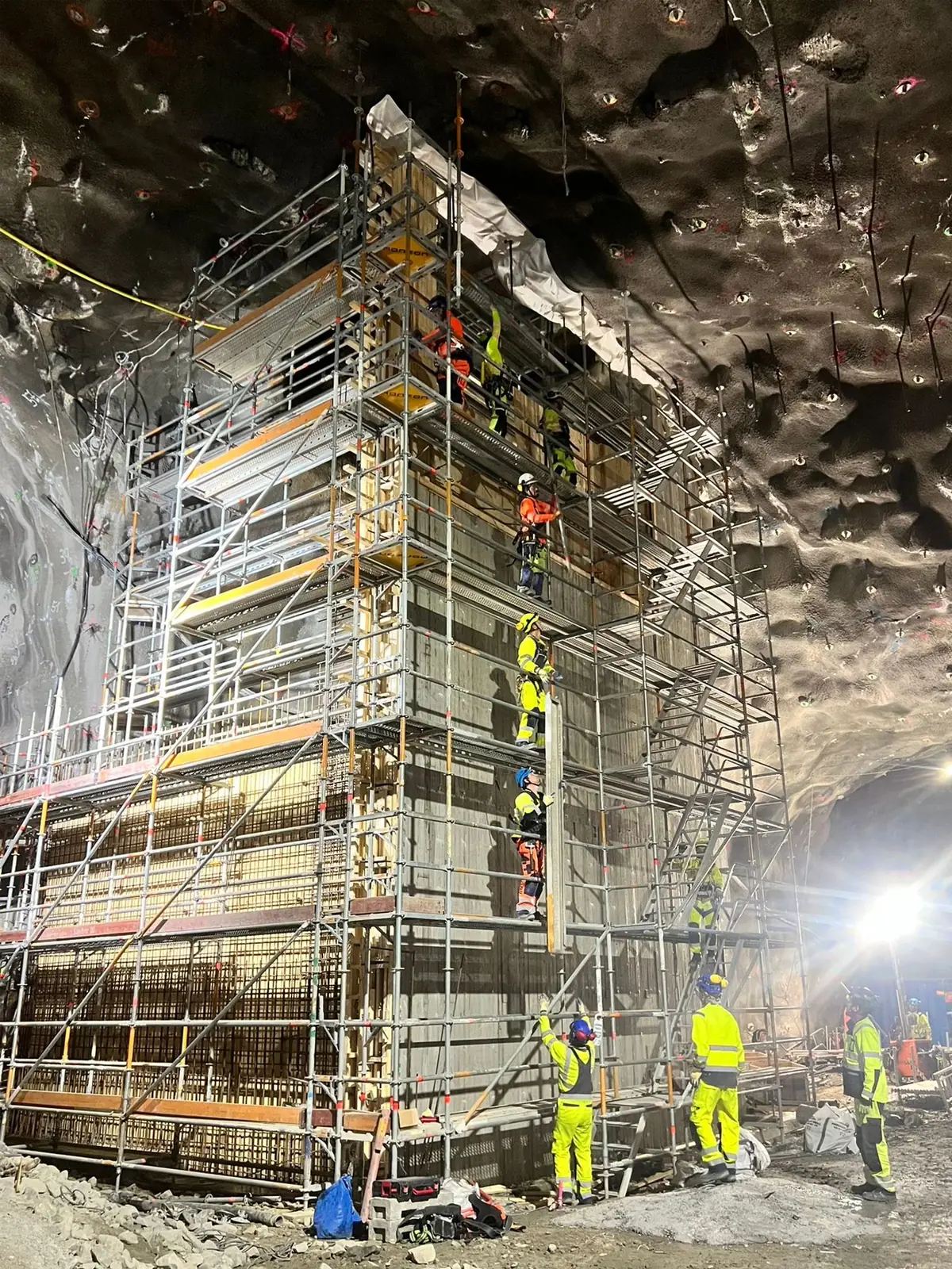 Högt ställningstorn vid en formvägg i ett bergrum, med arbetare på flera plan och på golvet nedanför