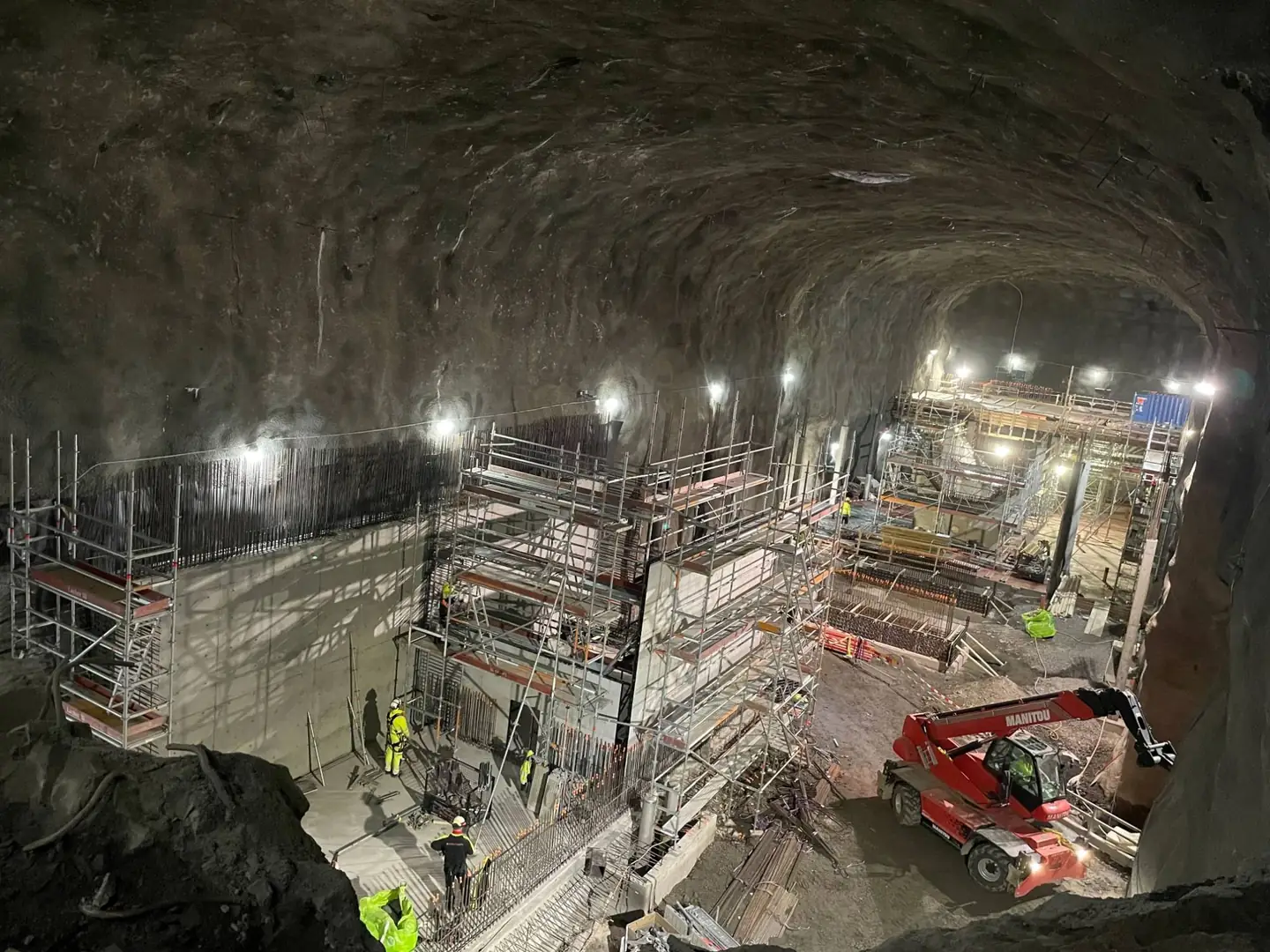 Bergrum under byggnad med armerade betongväggar, ställningar och en teleskoplastare