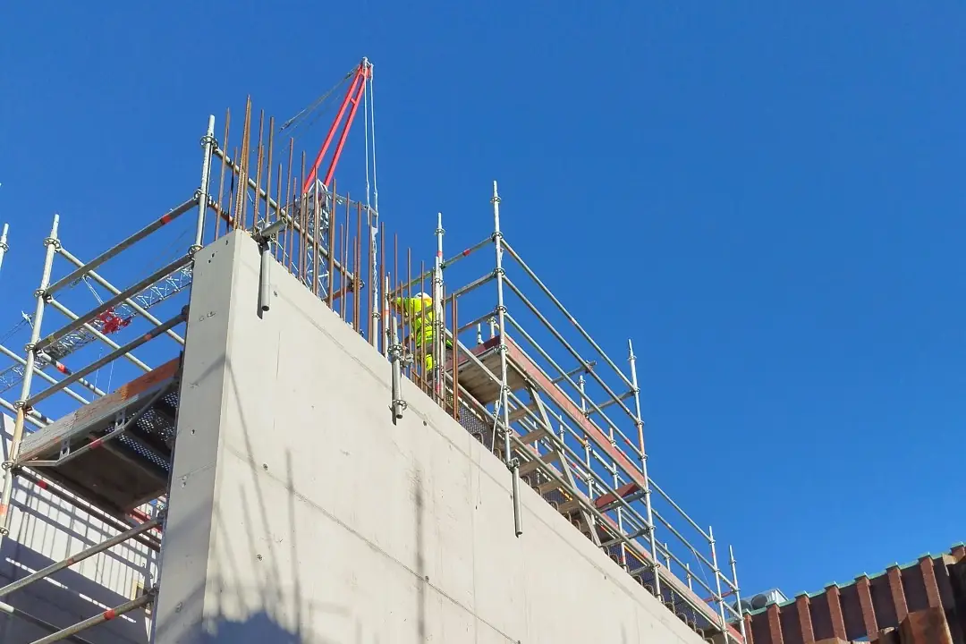 Nygjuten betongvägg med ställning och utstickande armering mot blå himmel